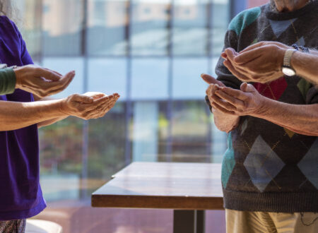 A close up of four people stood in a circle, with their hands outstretched towards eachother. The image is close up so we cannot see their heads. Two of them are men and two are women. They are in a light room.